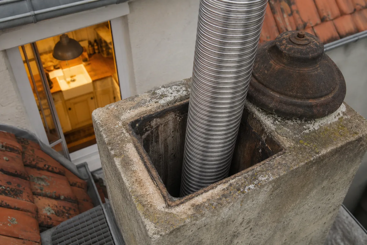 Tubage inox descendant dans un conduit de cheminée maçonné, vu depuis le toit