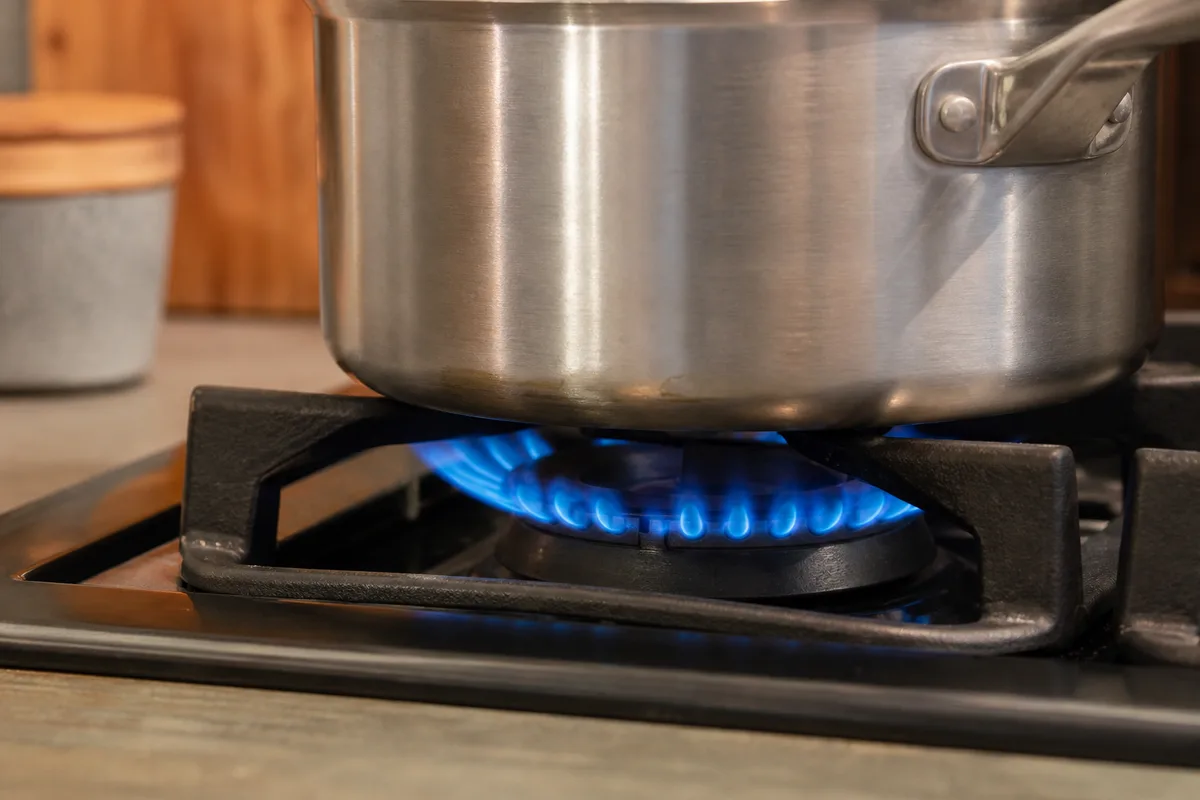 Brûleur de gazinière allumé, flamme bleue régulière sous une casserole en inox