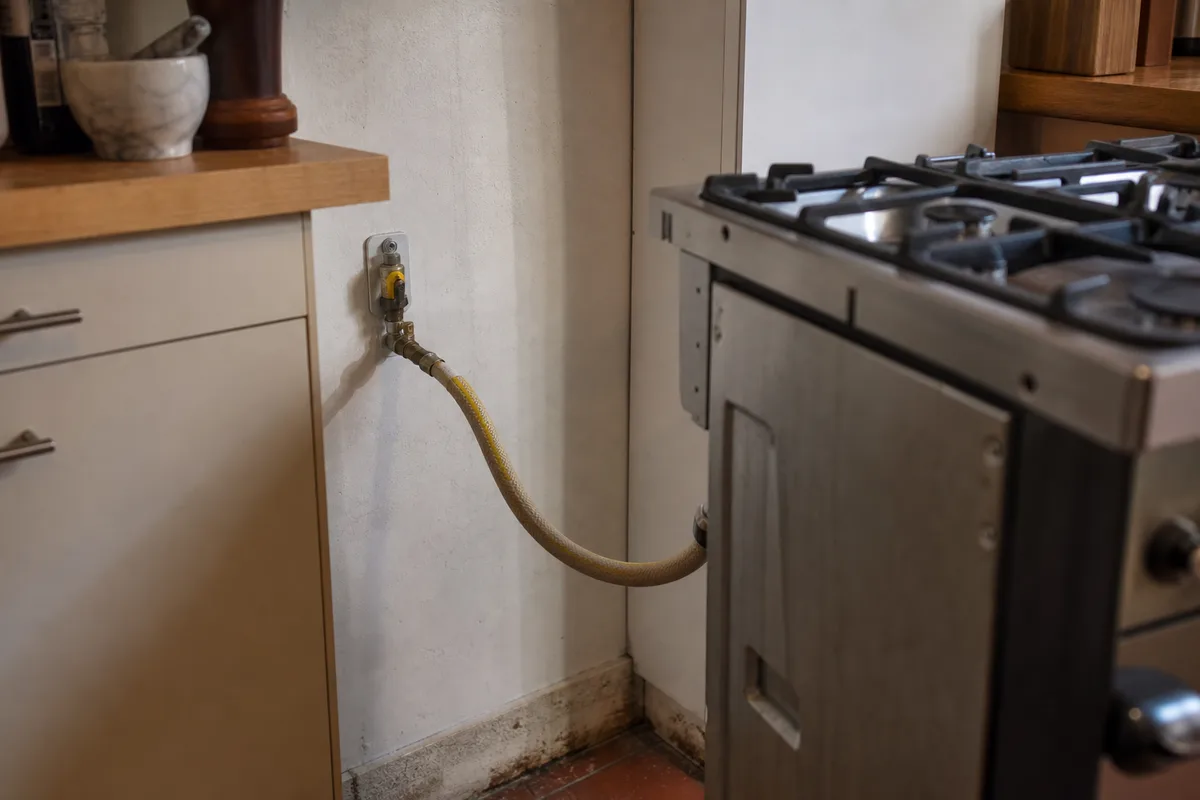 Robinet d’arrêt gaz mural et tuyau flexible derrière une cuisinière écartée du mur