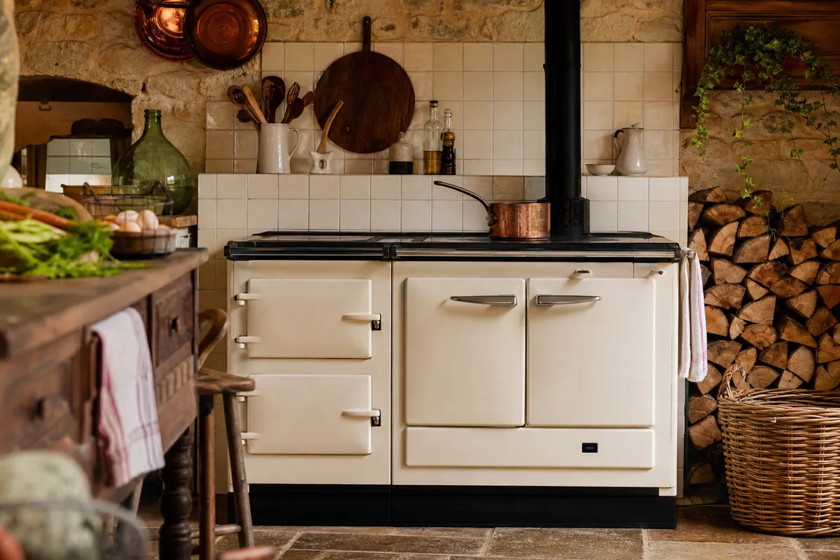 Cuisinière en fonte émaillée dans une cuisine de campagne, casserole en cuivre sur le foyer et bois empilé à côté